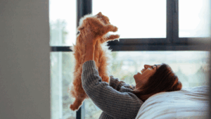 Woman lifting a fluffy orange cat in the air indoors.